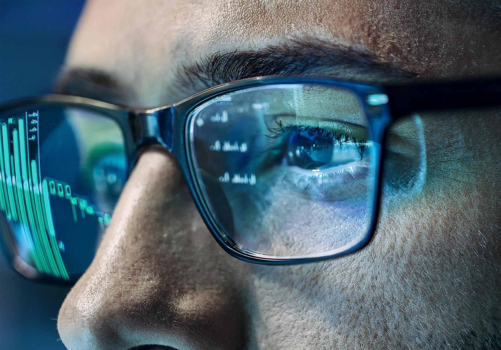 Close-up of eyes behind glasses, reflecting data on a screen